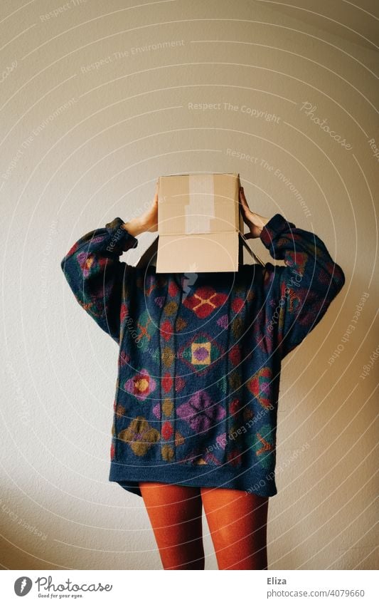 Frau in bunter Kleidung mit einem Karton auf dem Kopf Kiste verschicken bestellen anonym verstecken genervt Paket Schachtel Verpackung Pappkarton Pullover dsgvo