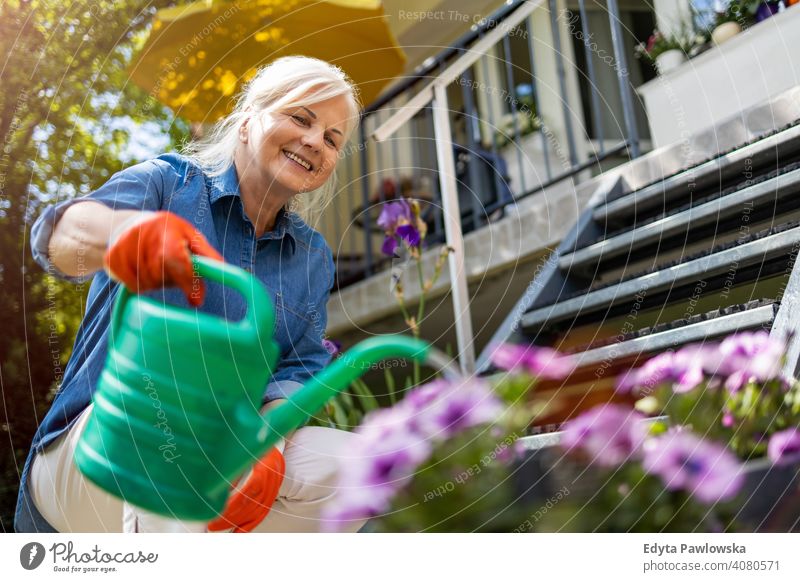 Ältere Frau bewässert Pflanzen in ihrem Garten Lächeln Glück genießend Positivität Vitalität Freude Selbstvertrauen Menschen Senior reif lässig Kaukasier älter