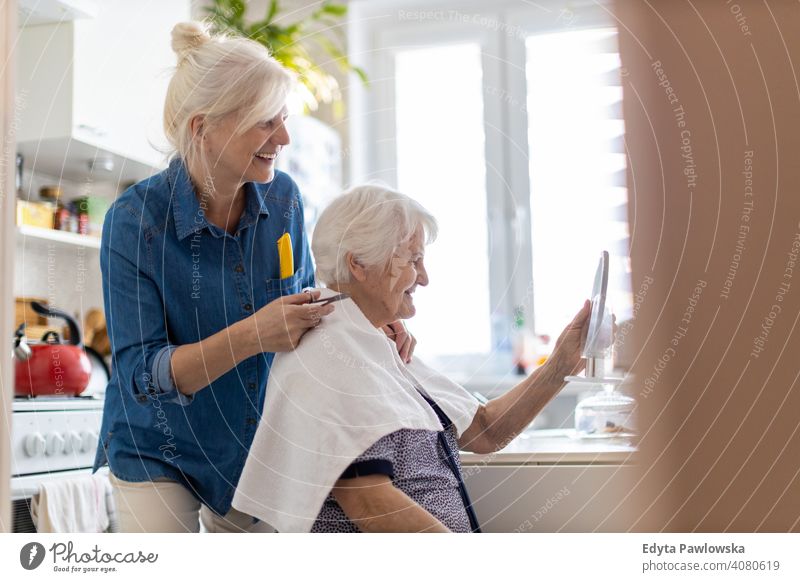 Frau schneidet ihrer älteren Mutter zu Hause die Haare Lächeln Glück Menschen Senior reif heimwärts alt häusliches Leben Großmutter Rentnerin Großeltern