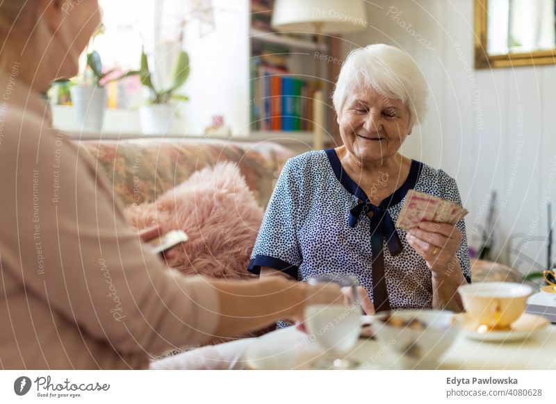 Ältere Frau und ihre erwachsene Tochter spielen Karten zu Hause Lächeln Glück genießend Positivität Vitalität Freude Selbstvertrauen Menschen Senior reif lässig
