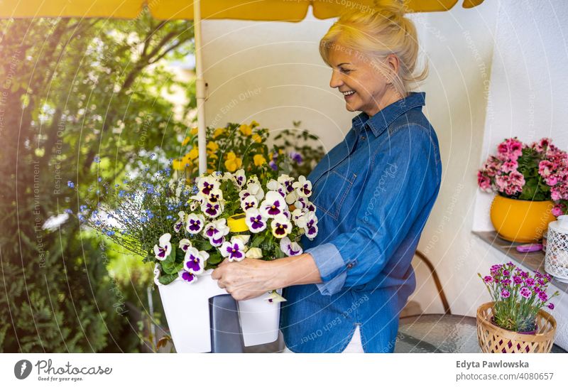 Seniorin, die sich um ihre Pflanzen auf dem Balkon kümmert Lächeln Glück genießend Positivität Vitalität Freude Selbstvertrauen Menschen Frau reif lässig