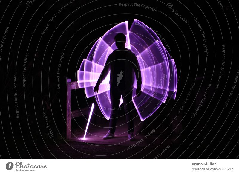 Silhouette eines Mannes stehend mit einem Lichtschwert mit Neon-Zeichnungen und Leds bei lightpainting Lichtmalerei Junge abstrakt Grafik u. Illustration
