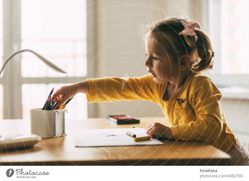 Ein kleines Mädchen zeichnet am Tisch mit Buntstiften zu Hause oder im Kindergarten. Kindheit, Kreativität, Bildung. Seitenansicht zeichnen wenig Bleistift