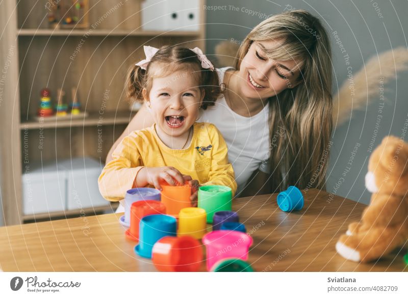 Mama und ein lachendes kleines Mädchen spielen mit bunten Förmchen am Tisch zu Hause. Gemeinsame Zeit, Mutterschaft, Elternschaft Kind heimwärts Spiel Formen