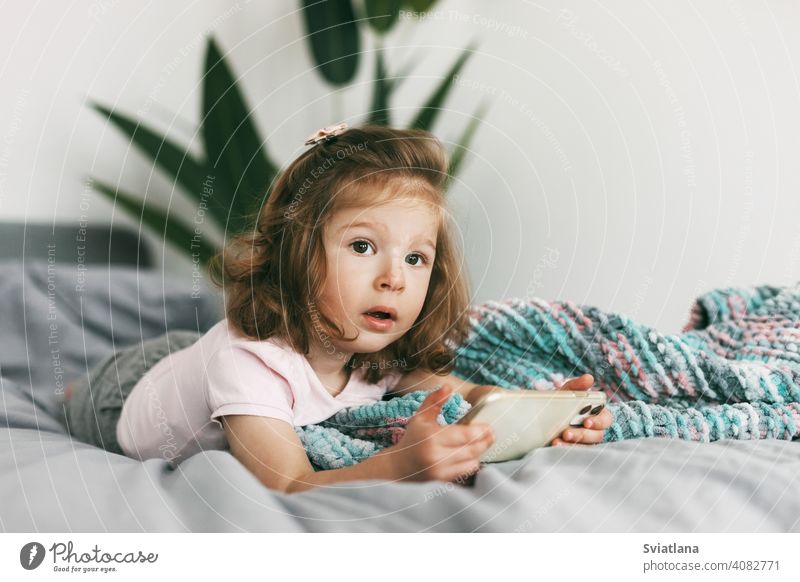Porträt eines charmanten kleinen Mädchens, das vor dem Schlafengehen Cartoons auf ihrem Telefon ansieht. Kindheit, glückliche Zeit, Pflege Smartphone Bett