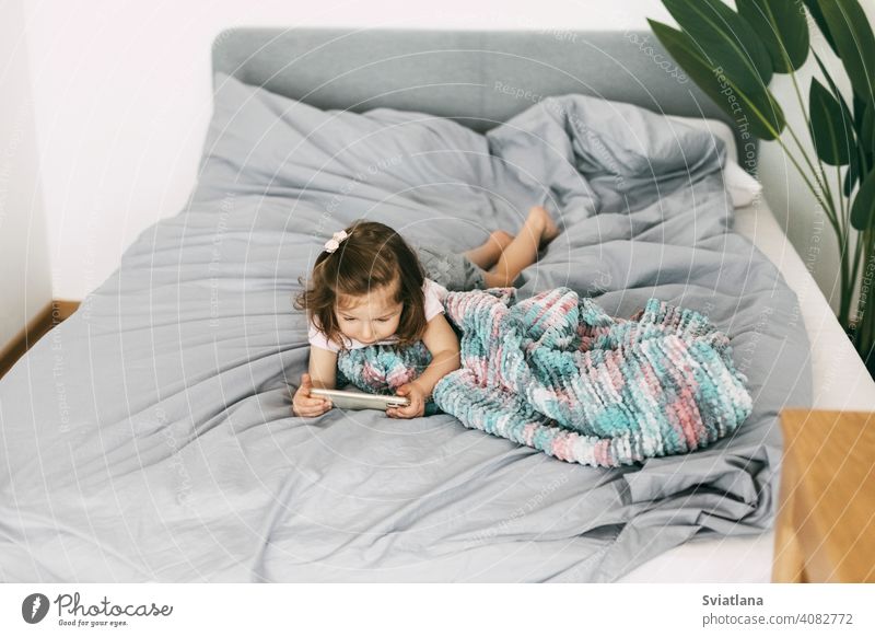 Ein kleines Mädchen schaut Cartoons auf ihrem Telefon oder spielt auf dem Bett, bevor es ins Bett geht. Ansicht von oben Smartphone Kind Mobile heimwärts