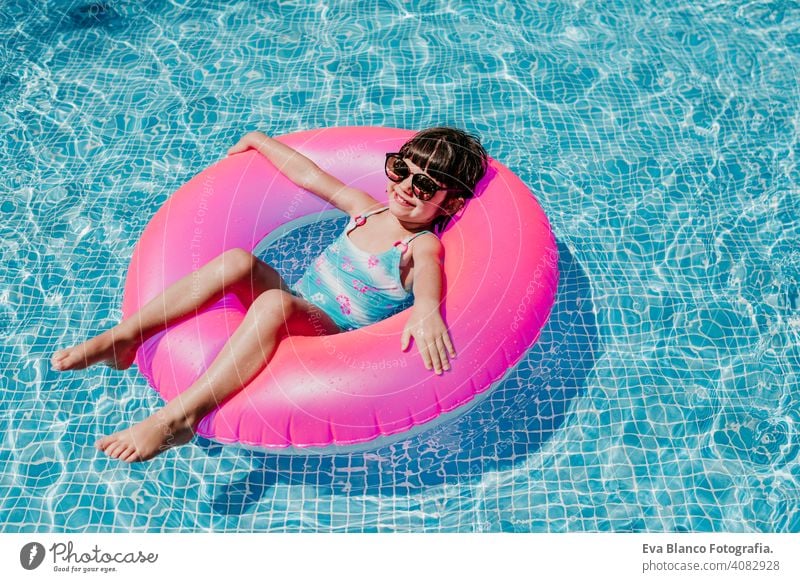 schönes Kind Mädchen schwimmt auf rosa Donuts in einem Pool. Tragen Sie eine Sonnenbrille und lächelnd. Spaß und Sommer Lebensstil Aktivität Schönheit im Freien