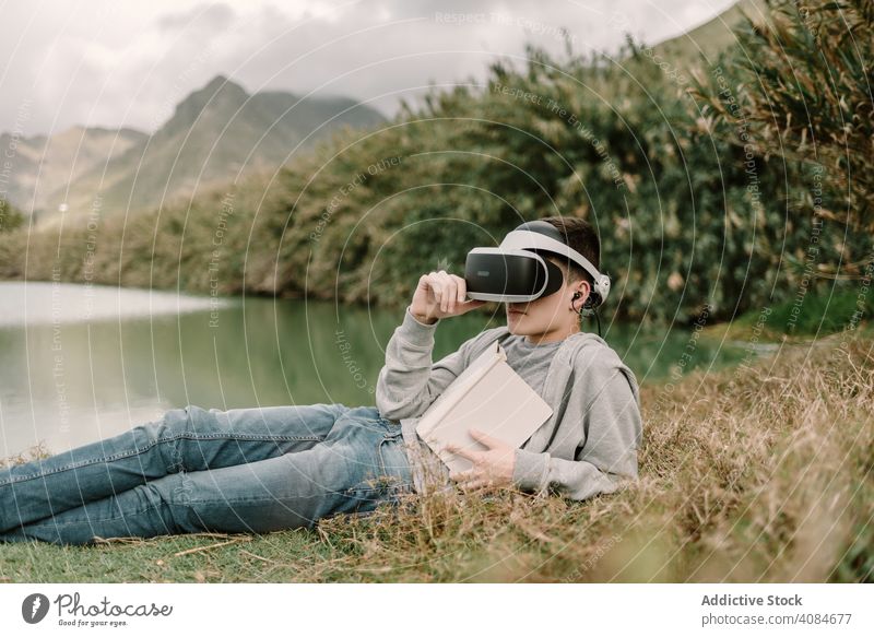 Junger Teenager mit Virtual-Reality-Brille beim Lesen im Freien virtuell Realität lehrreich VR Jugendlicher Natur Headset Technik & Technologie futuristisch 3d