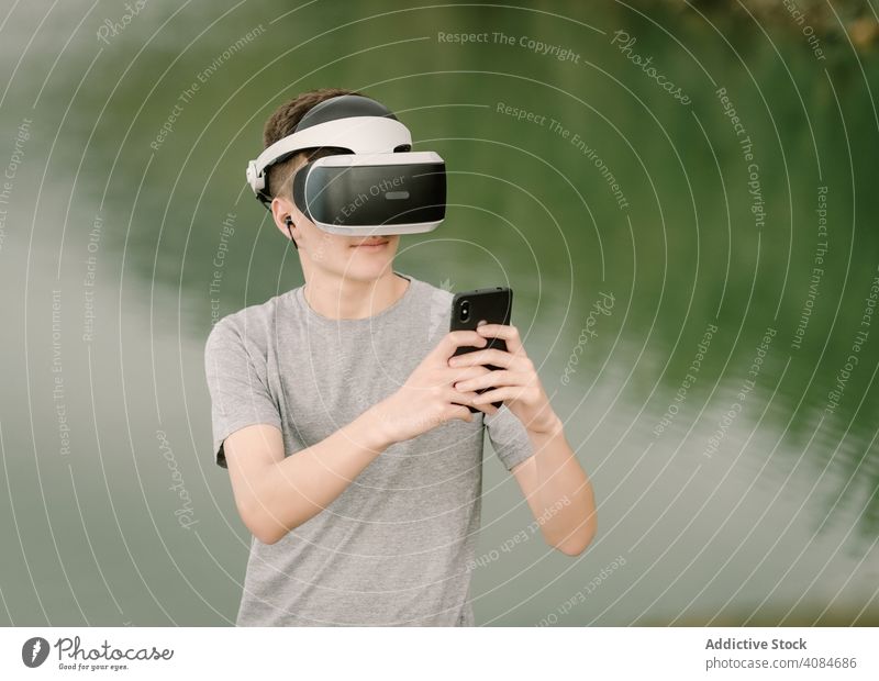 Junger Teenager mit Virtual-Reality-Brille und Smartphone im Freien virtuell Realität VR Jugendlicher Telefon Natur Stehen Headset Technik & Technologie Spiel