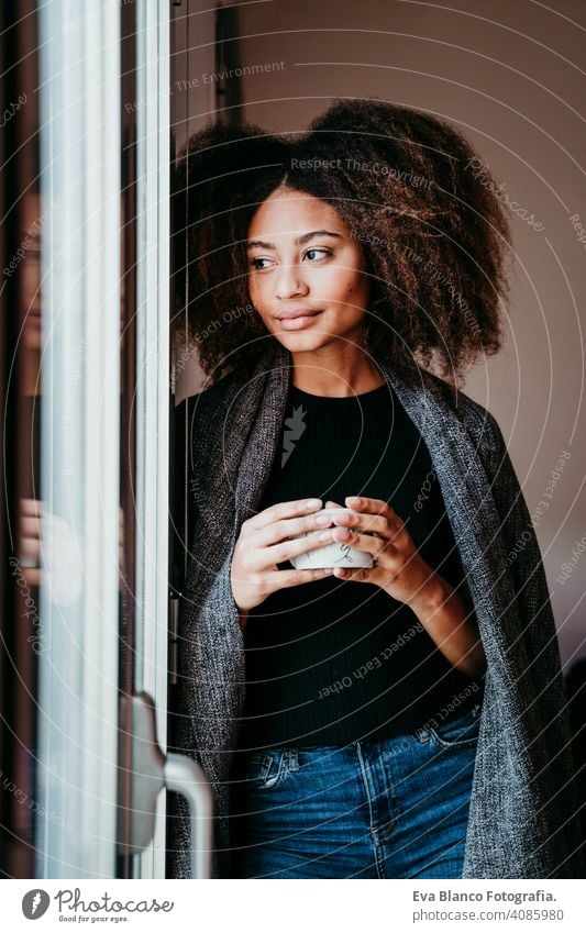 Porträt einer schönen afroamerikanischen jungen Frau am Fenster mit einer Tasse Kaffee in der Hand. Lebensstil im Haus Afroamerikaner heimwärts ethnisch