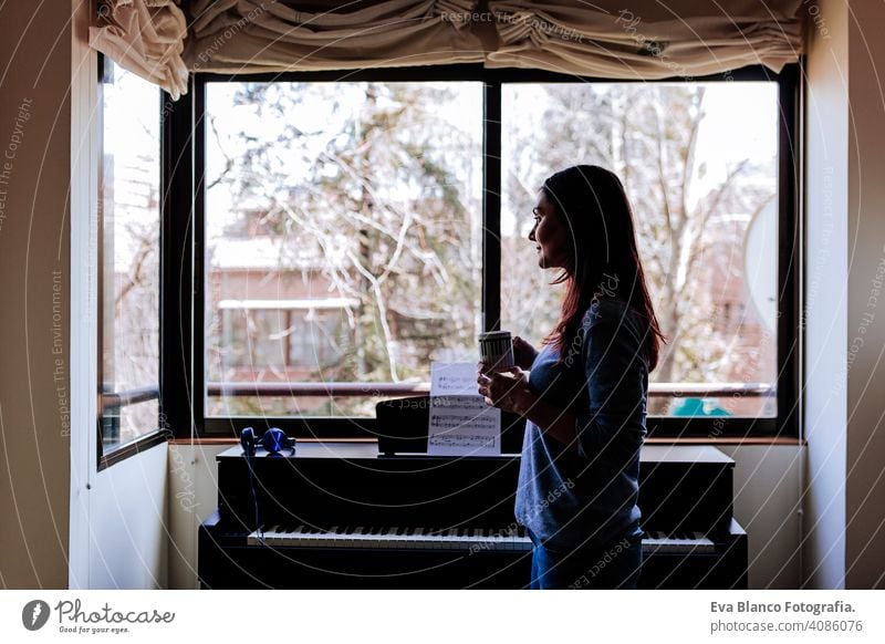junge Frau hält eine Tasse Kaffee und bereit, Klavier zu spielen, indem sie ein Notenblatt liest. Musik-Konzept im Innenbereich Stil menschlich Taste Hinweis