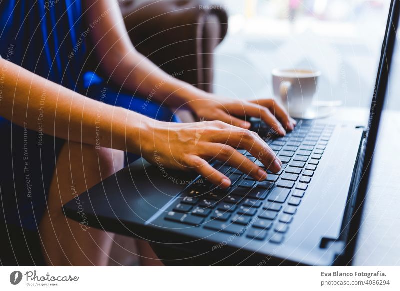 Draufsicht auf eine junge schöne Frau, die am Laptop schreibt, daneben Kaffee. Lässiges blaues Kleid. Modernes Leben im Innenbereich Hipster Hochschule Computer