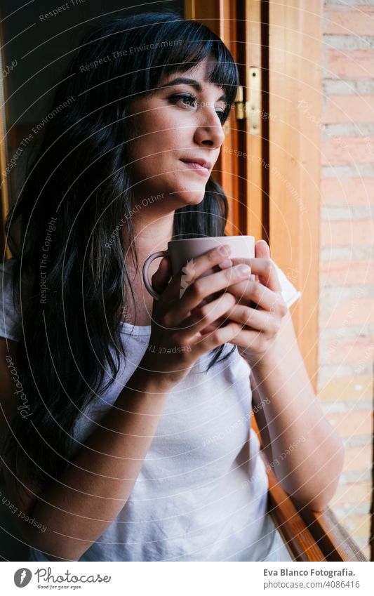 junge kaukasische Frau zu Hause am Fenster mit einer Tasse Kaffee oder Tee. Morgen und entspannen Konzept. Lebensstil im Innenbereich Mädchen bequem