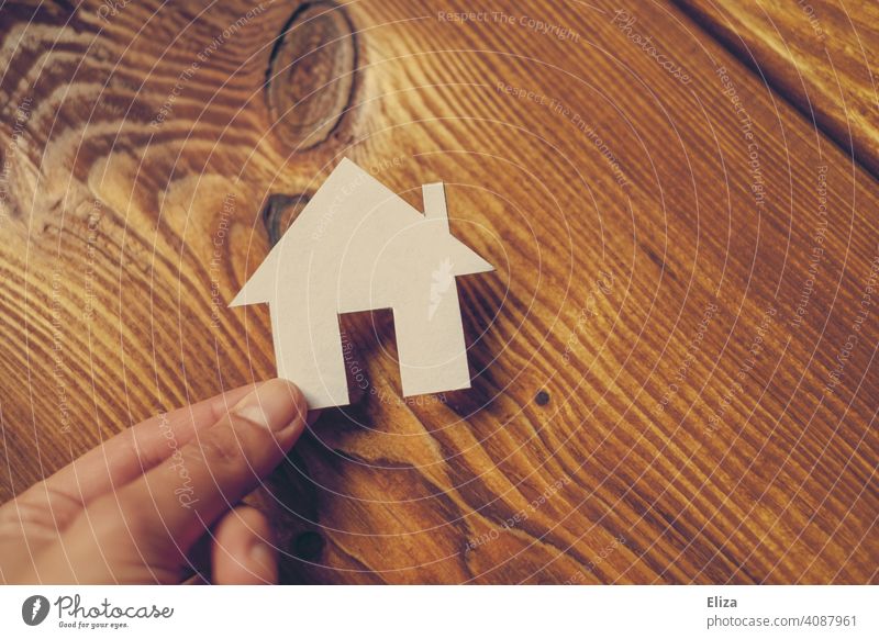 Eine Hand hält ein Haus aus Papier. Eigenheim und Hausbau. Zuhause Traumhaus Holz Haus bauen häuslich Immobilie immobilien Gebäude wohnen zuhause Person Mensch
