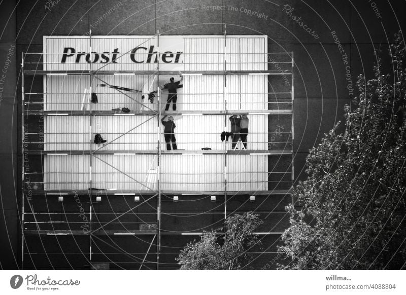 Ein Plakat wird angebracht auf einem Gerüst am Plattenbau - Prost Cher Plakatkleber Hauswand Plakatwand plakatieren Werbung Menschen Männer