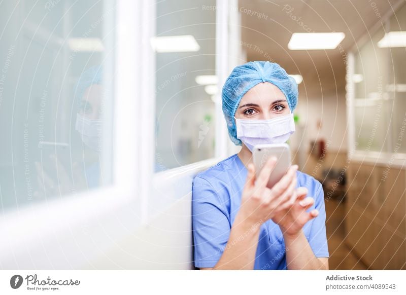 Weibliche Chirurgin benutzt ihr Smartphone in einem Krankenhaus Job Körperhaltung überdrüssig im Innenbereich Hut Wand Operationssaal professionell