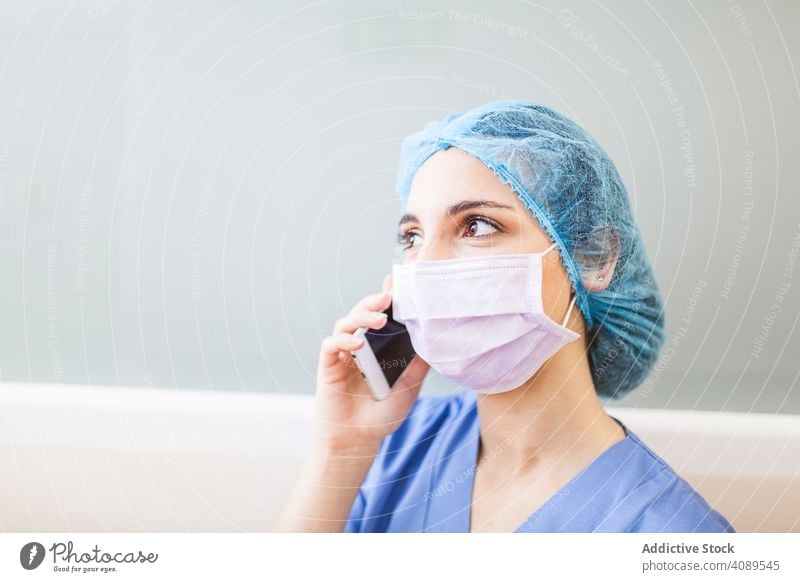 Weibliche Chirurgin benutzt ihr Smartphone in einem Krankenhaus Job Körperhaltung überdrüssig im Innenbereich Hut Wand Operationssaal professionell Flur weiß