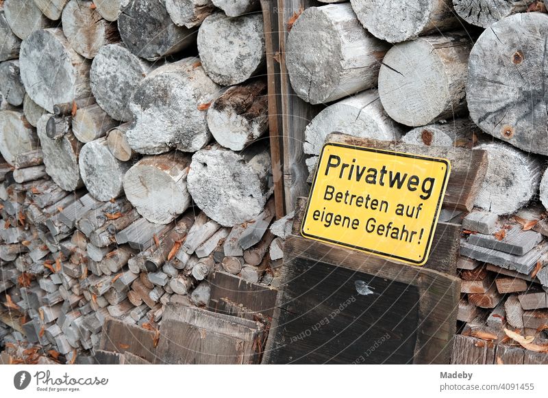 Gelbes Blechschild mit Warnhinweis vor gestapeltem Brennholz vor einem alten Bauernhaus im Herbst in Rudersau bei Rottenbuch im Kreis Weilheim-Schongau in Oberbayern