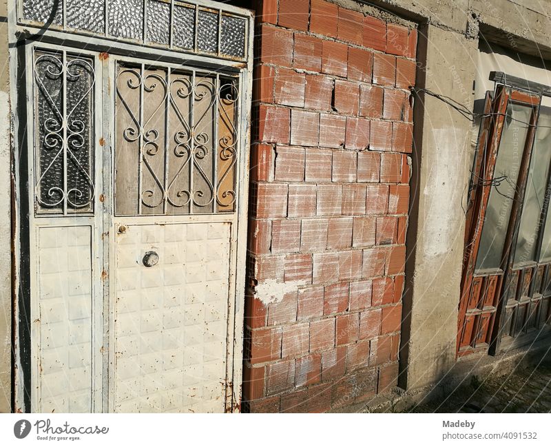 Alte leerstehende Werkstatt mit Tür aus Schmiedeeisen und unverputztem Backstein im Sonnenschein in Alacati bei Cesme am Mittelmeer in der Provinz Izmir in der Türkei