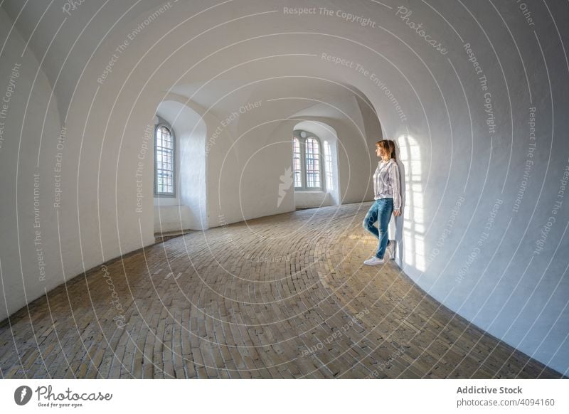 Lässige Frau, die sich in einer geräumigen Galerie mit Fenstern an die Wand lehnt Empore beobachten reisen Architektur Schatten Innenbereich anlehnen Windstille