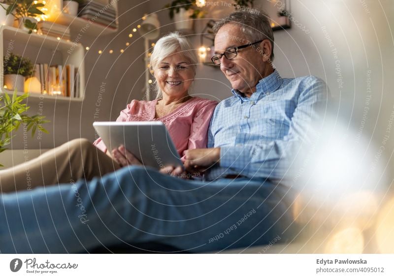 Reifes Paar verwendet ein Tablet beim Entspannen zu Hause Menschen Frau Erwachsener Senior reif lässig attraktiv männlich Mann Lächeln Glück Kaukasier