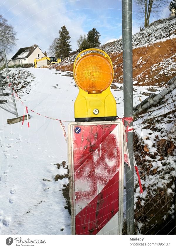 Warnbake mit rotem Graffiti und gelber Blinkleuchte im Winter mit Schnee auf einer Baustelle in Oerlinghausen bei Bielefeld am Hermannsweg im Teutoburger Wald in Ostwestfalen-Lippe