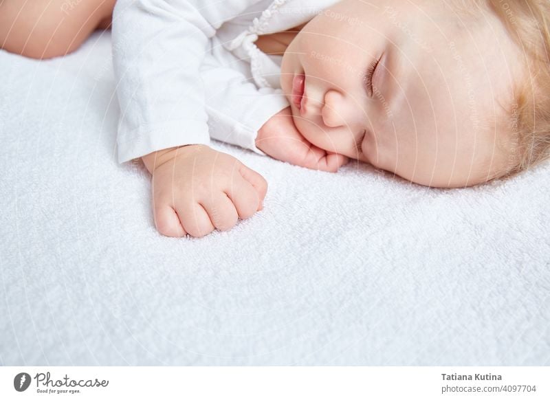 Niedliches Baby schläft süß auf weißer Bettwäsche in weißer Kleidung. Nahaufnahme. Schöne gesunde weiche Haut, lange Wimpern. Kind niedlich schlafen wenig
