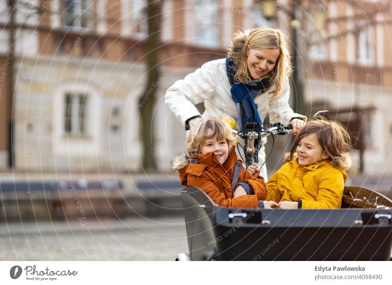 Mutter, die nach ihren Kindern schaut, die im vorderen Teil eines Lastenfahrrads fahren Lastenrad Fahrrad Fahrradfahren Verkehr Dreirad Gesundheit aktiv Zyklus