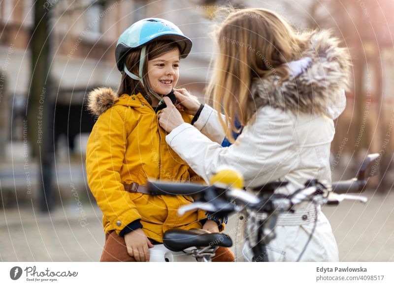 Mutter setzt ihrem Sohn einen Fahrradhelm auf jung tragend Schutzhelm Fahrradfahren Winter Frau Herbst Familie Eltern Verwandte Junge Kind Kinder Partnerschaft