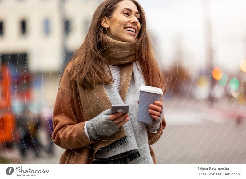 Lächelnde junge Frau mit Smartphone und Kaffeetasse im Freien in städtischer Umgebung Herbst fallen Mädchen schön Wetter Mantel Mode hübsch attraktiv