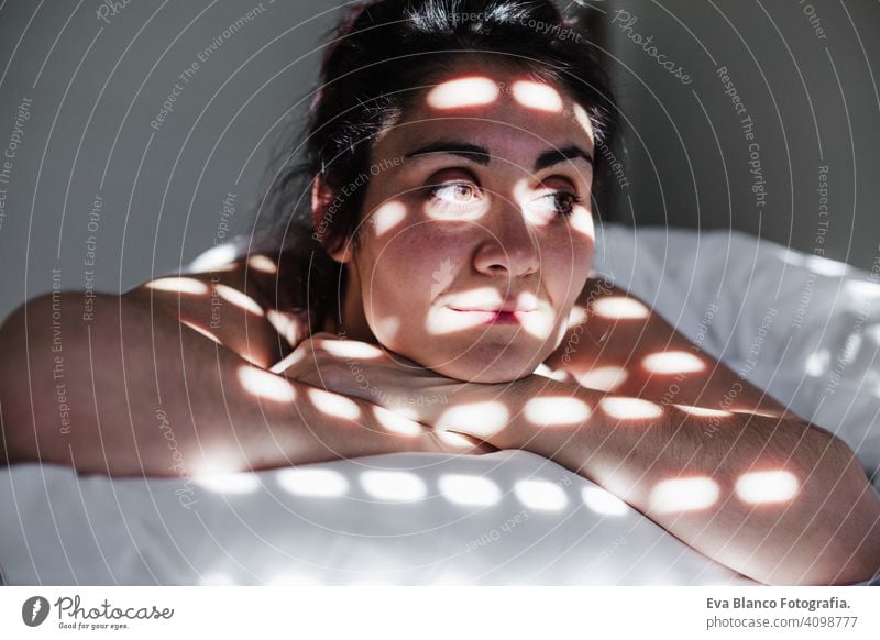 Porträt der attraktiven jungen kaukasischen Frau entspannt im Bett während der Morgenzeit. Lady genießt frische weiche Bettwäsche Bettwäsche und Matratze im Schlafzimmer. Blinde Schatten auf dem Gesicht