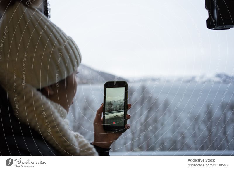 Ruhige Frau, die mit ihrem Smartphone ein Video der winterlichen Landschaft aufnimmt, während sie aus dem Fenster schaut Fotografie Winter Norwegen ersfjordbotn