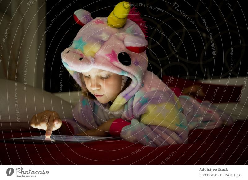 Mädchen mit Tablette auf dem Bett kigurumi Einhorn Decke Tierhaut benutzend zuschauend Spielen Schlafenszeit Pyjama Lügen Kind Glück Spaß positiv genießen rot