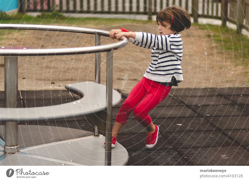 Seitenansicht eines kleinen Mädchens, das ein sich drehendes Karussell auf einem Spielplatz antreibt aktiv Aktivität Beweglichkeit Vergnügen amüsant Kaukasier