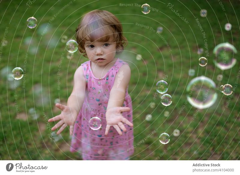 Fröhliches Mädchen spielt mit bunten Blasen im Gras Seife Kindheit freudig Spaß bezaubernd Spielen heiter Park spielerisch Genuss Aktion nass wenig Bewegung