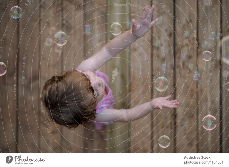 Fröhliches Mädchen spielt mit bunten Seifenblasen im Holzboden Blasen Kindheit freudig Spaß bezaubernd Spielen heiter Park spielerisch Genuss Aktion nass wenig