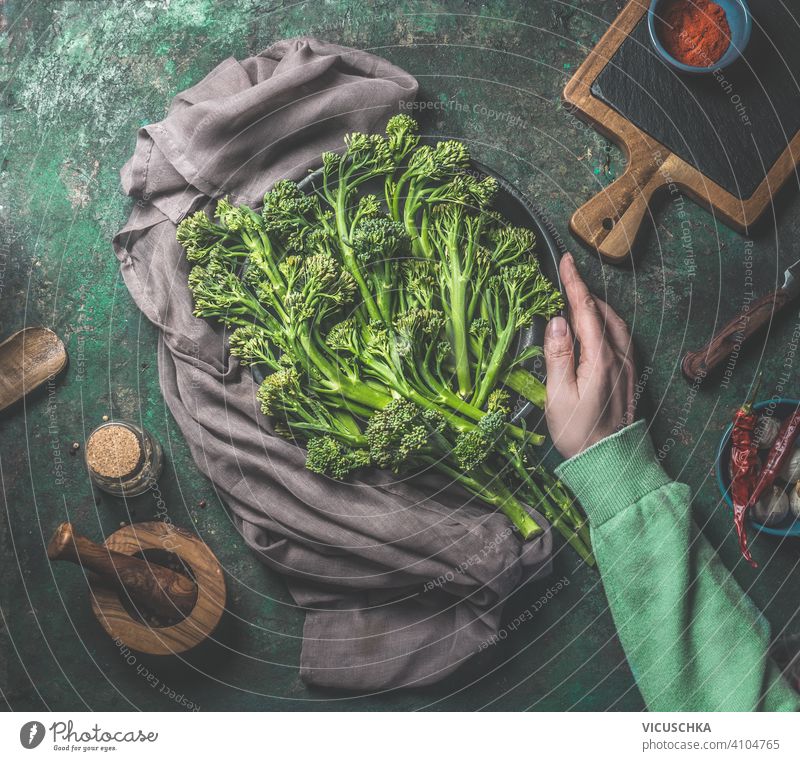 Frauenhand in grünem Sweatshirt hält wilden Brokkoli auf dunklem rustikalem Hintergrund. Ansicht von oben. Gesundes Essen Hand Beteiligung dunkel Draufsicht
