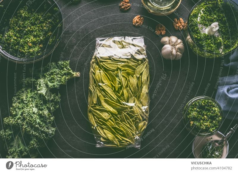 Grüne Nudeln in Plastikverpackung auf dunklem Küchentisch mit Grünkohl und anderen Zutaten. Ansicht von oben grün Spätzle Kunststoffverpackung dunkel Tisch Kale