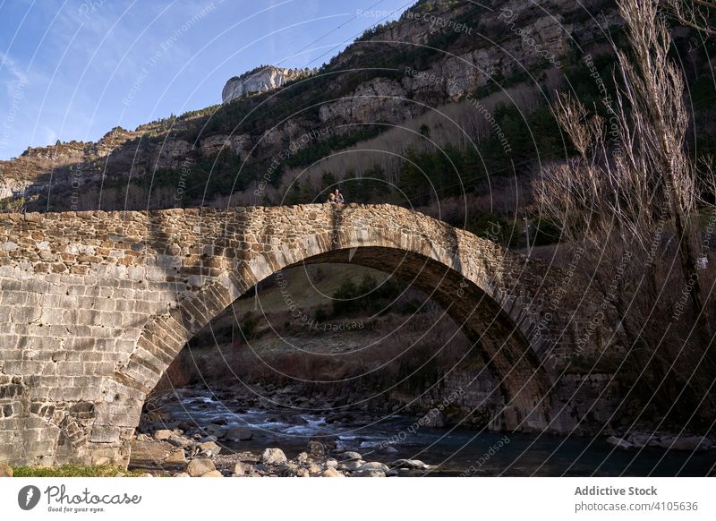 Menschen stehen auf einer alten Brücke über einem kleinen Fluss in einem Bergtal Tal Wald antik Struktur Architektur Wasser felsig Landschaft Stein