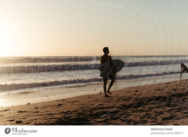 Unbekannter männlicher Surfer bei Sonnenuntergang am Strand Spaziergang Mann Surfbrett Meeresufer Sommerzeit Wasser Surfen MEER winken Gerät extrem aktiv Sport