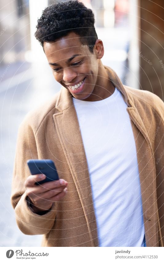 Junger schwarzer Mann, der sein Smartphone im Freien benutzt. männlich Kubaner jung Person Lächeln Glück Schüler Telefon lässig Lifestyle klug T-Shirt