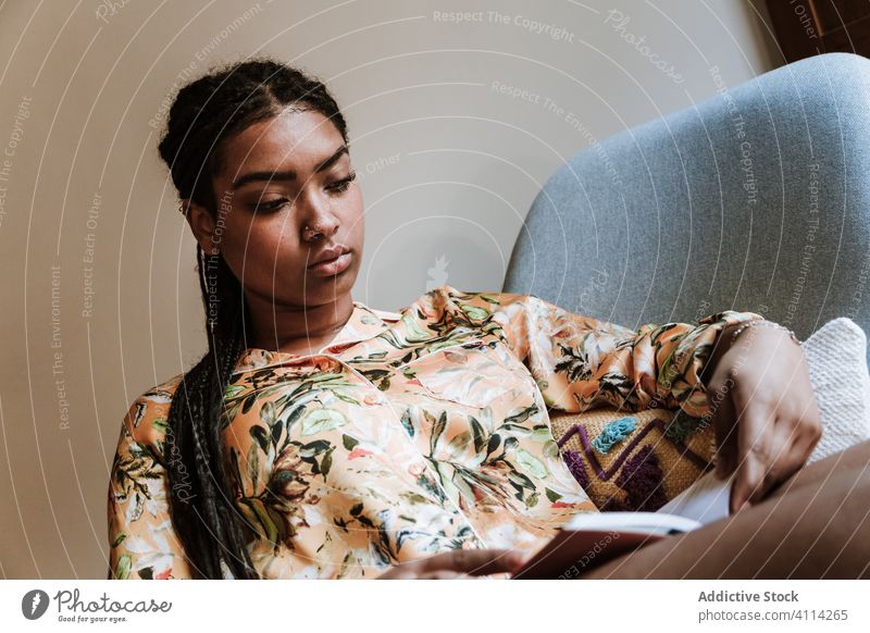 Ethnische Frau mit zu Hause ruhendem Buch heimwärts lesen Afrikanisch Amerikaner schwarz lässig Stuhl brünett Windstille Sitzen jung gemütlich ethnisch Piercing