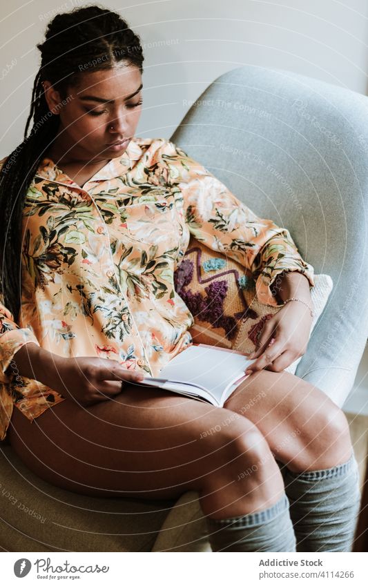 Ethnische Frau mit zu Hause ruhendem Buch heimwärts lesen lässig Stuhl Windstille jung gemütlich ethnisch Freizeit sich[Akk] entspannen Lifestyle sitzen