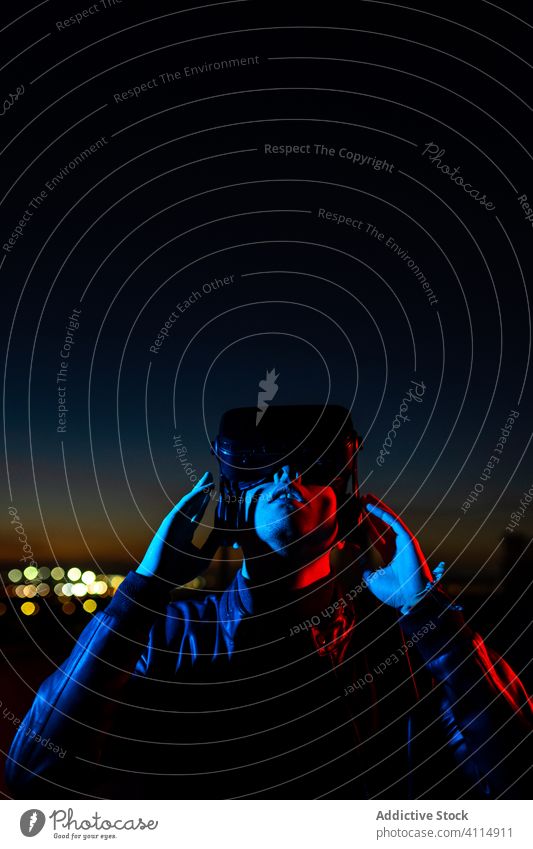 Junger Mann erforscht virtuelle Realität Nacht VR dunkel Straße Headset Schutzbrille futuristisch leuchten neonfarbig rot Licht männlich modern Gerät Apparatur