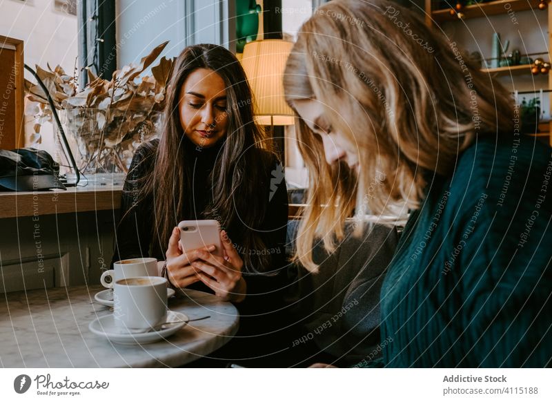 Freundinnen ruhen sich in gemütlichem Cafe aus Frauen Café Zusammensein Kaffee Smartphone benutzend Witz lässig Wochenende jung Sitzung Restaurant trinken Tasse