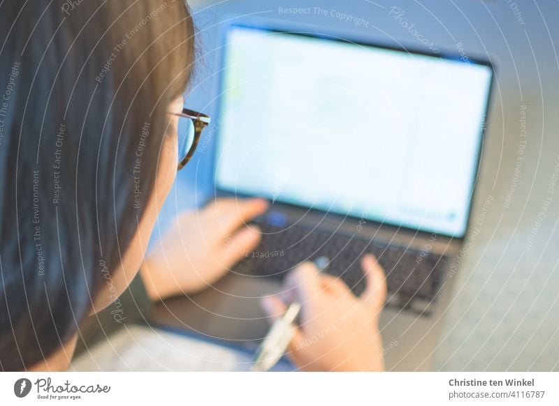 Blick über die Schulter einer jungen Frau mit Brille, die zu Hause am Notebook arbeitet. Homeoffice. Online-Vorlesung. Homeschooling. Laptop Computer junge Frau