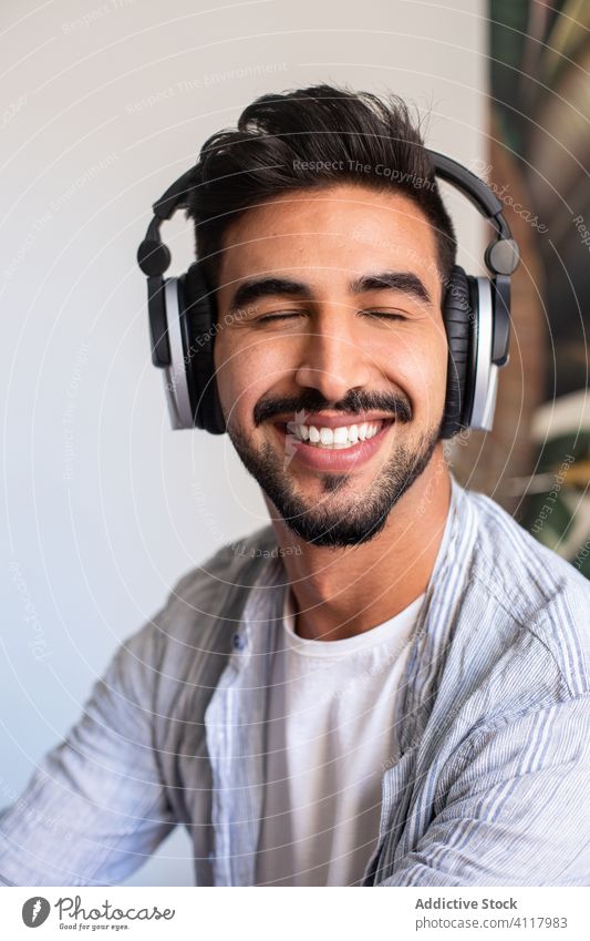 Bärtiger Mann hört mit geschlossenen Augen Musik zuhören Lächeln heimwärts Kopfhörer ethnisch Glück ruhen Wochenende männlich Headset heiter Klang Vollbart Spaß