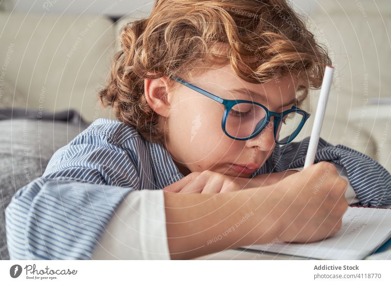 Junge macht Hausaufgaben am runden Tisch heimwärts lernen schreiben Notizblock Wohnzimmer klug Kind Komfort Sofa Liege lässig elementar Quarantäne