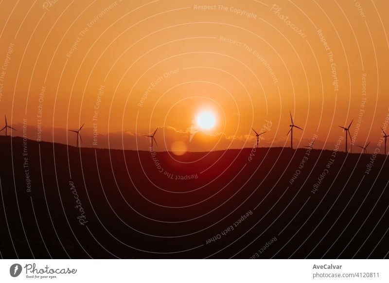 Silhouetten von einigen Windmühlen auf der Spitze eines Berges während einer super orange Sonnenuntergang mit Kopie Raum friedlich Pflanze Energie regenerativ