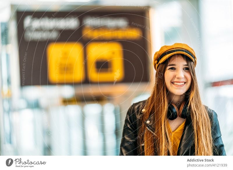 Trendige junge Frau im modernen Flughafenterminal Tourist trendy Passagier heiter Terminal Kopfhörer Stil Mode Abheben Lächeln Ausflug Handgriff warten schwarz